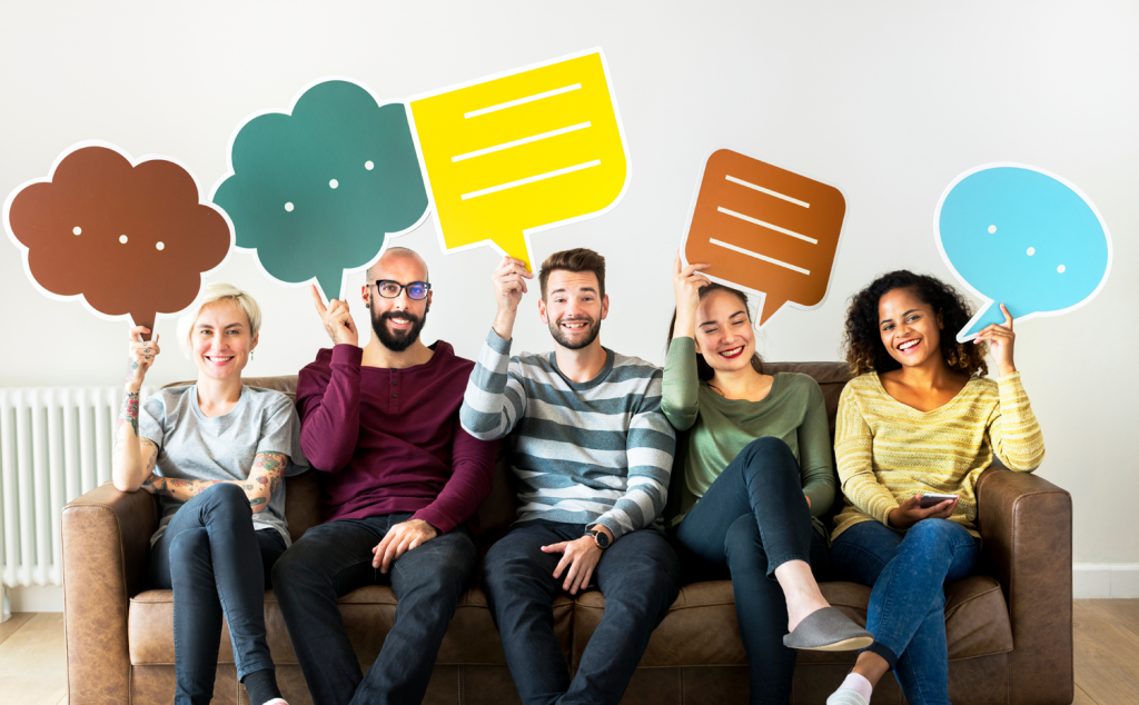 Five young people seated on a couch with each holding up large cardboard speech bubble cutouts above their heads