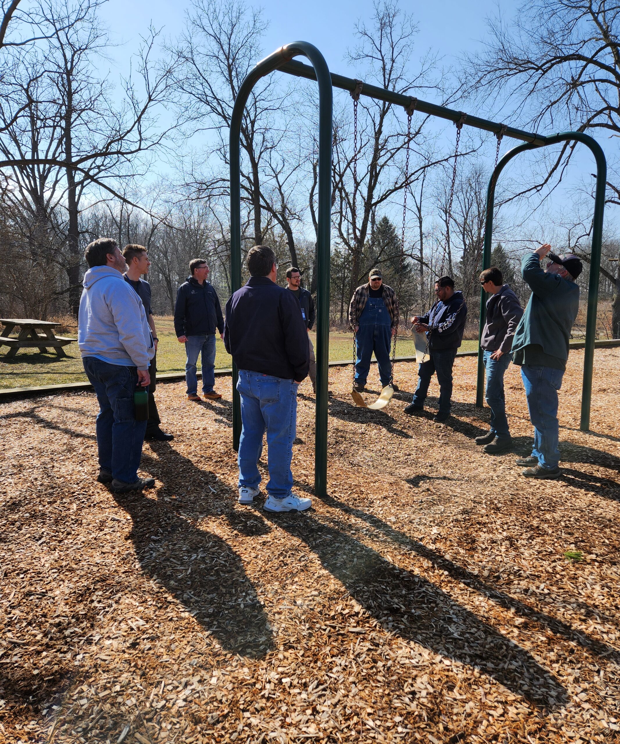 A group of people standing around a swing set on a park playground